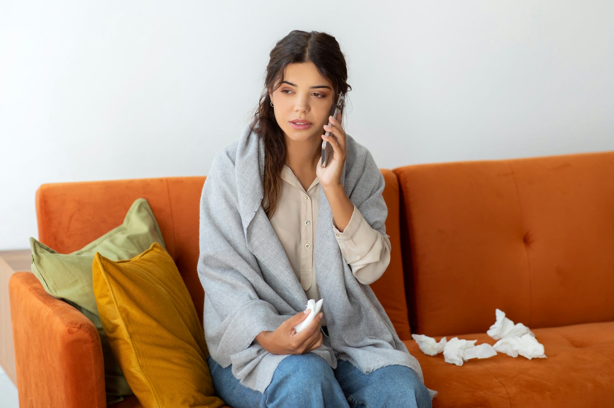 Concerned young woman wrapped in blanket making phone call to doctor