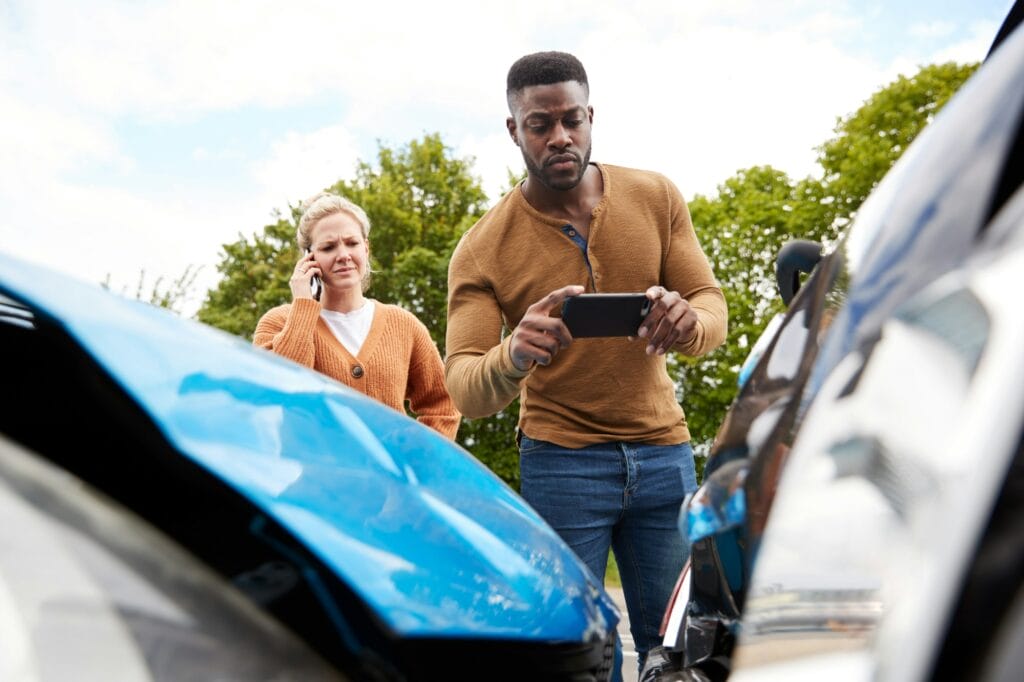 Male Motorist Involved In Car Accident Taking Picture Of Damage For Insurance Claim